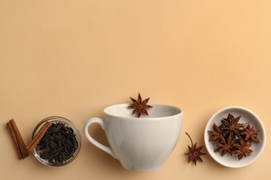 Cup with anise stars, dry tea and cinnamon sticks on beige background, flat lay. Space for text