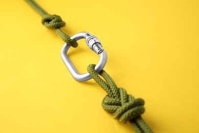 Photo of One metal carabiner with ropes on yellow background, closeup