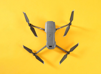 Photo of Modern drone with camera on yellow background, top view. Space for text