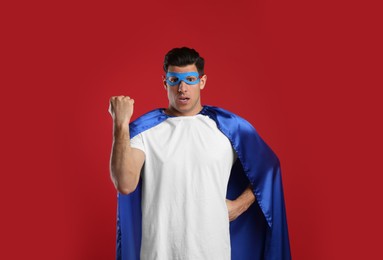 Photo of Emotional man wearing superhero cape and mask on red background