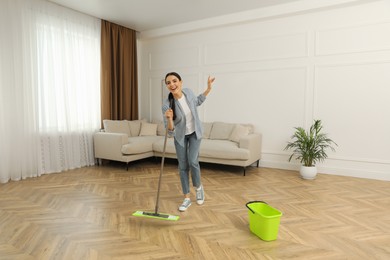 Photo of Woman having fun while cleaning floor with mop at home