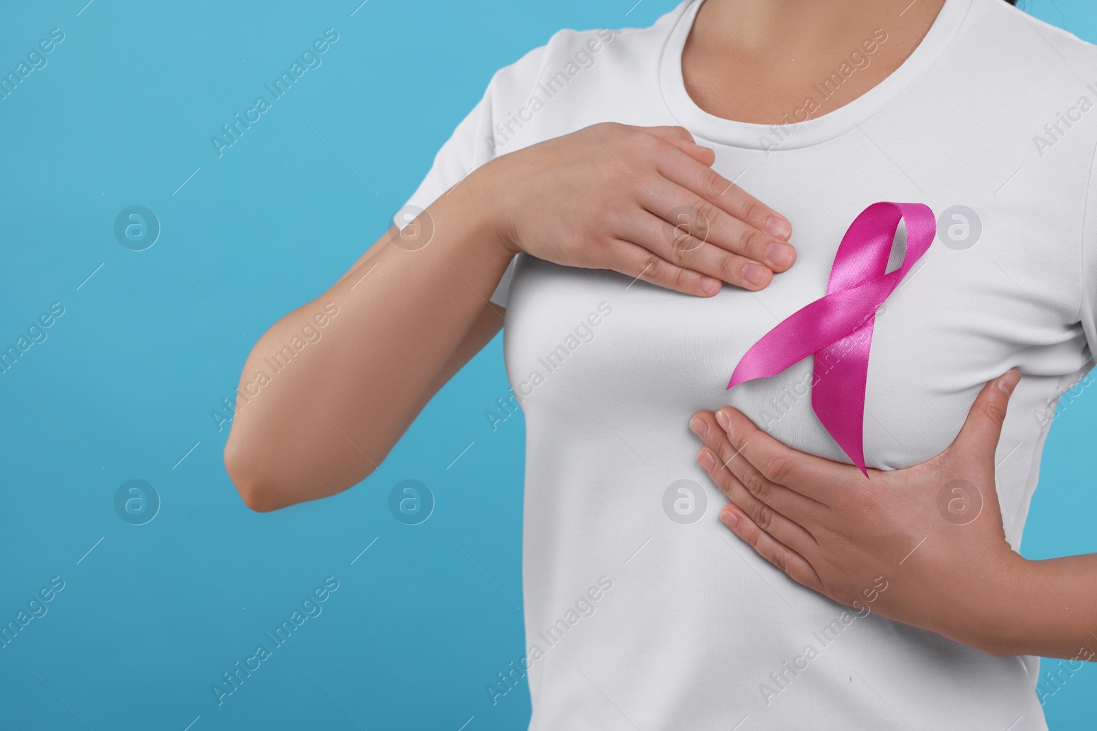 Photo of Woman with pink ribbon on light blue background, closeup. Breast cancer awareness