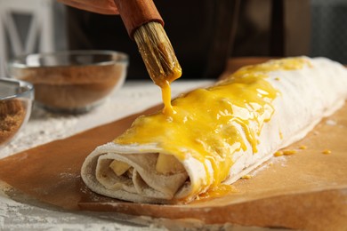 Spreading egg yolk onto delicious raw apple strudel at table, closeup