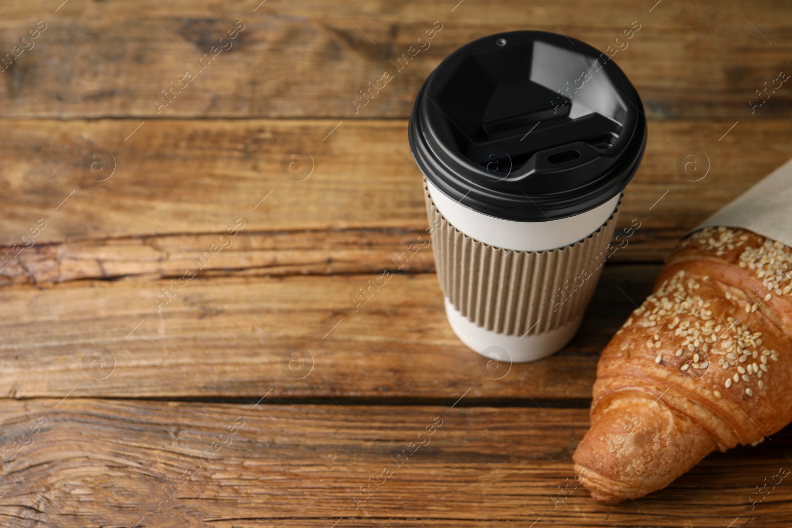 Photo of Coffee to go. Paper cup with tasty drink and croissant on wooden table. Space for text