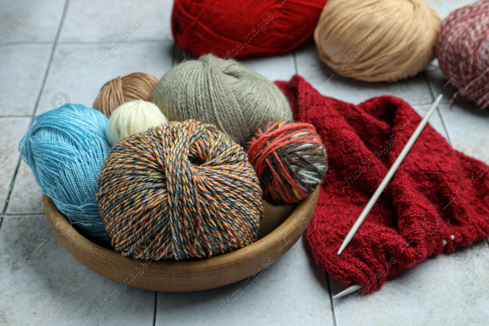 Photo of Soft woolen yarns, knitting and needles on grey tiled background