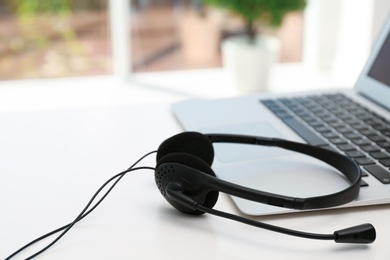 Photo of Modern laptop and headset on table indoors. Technical support concept