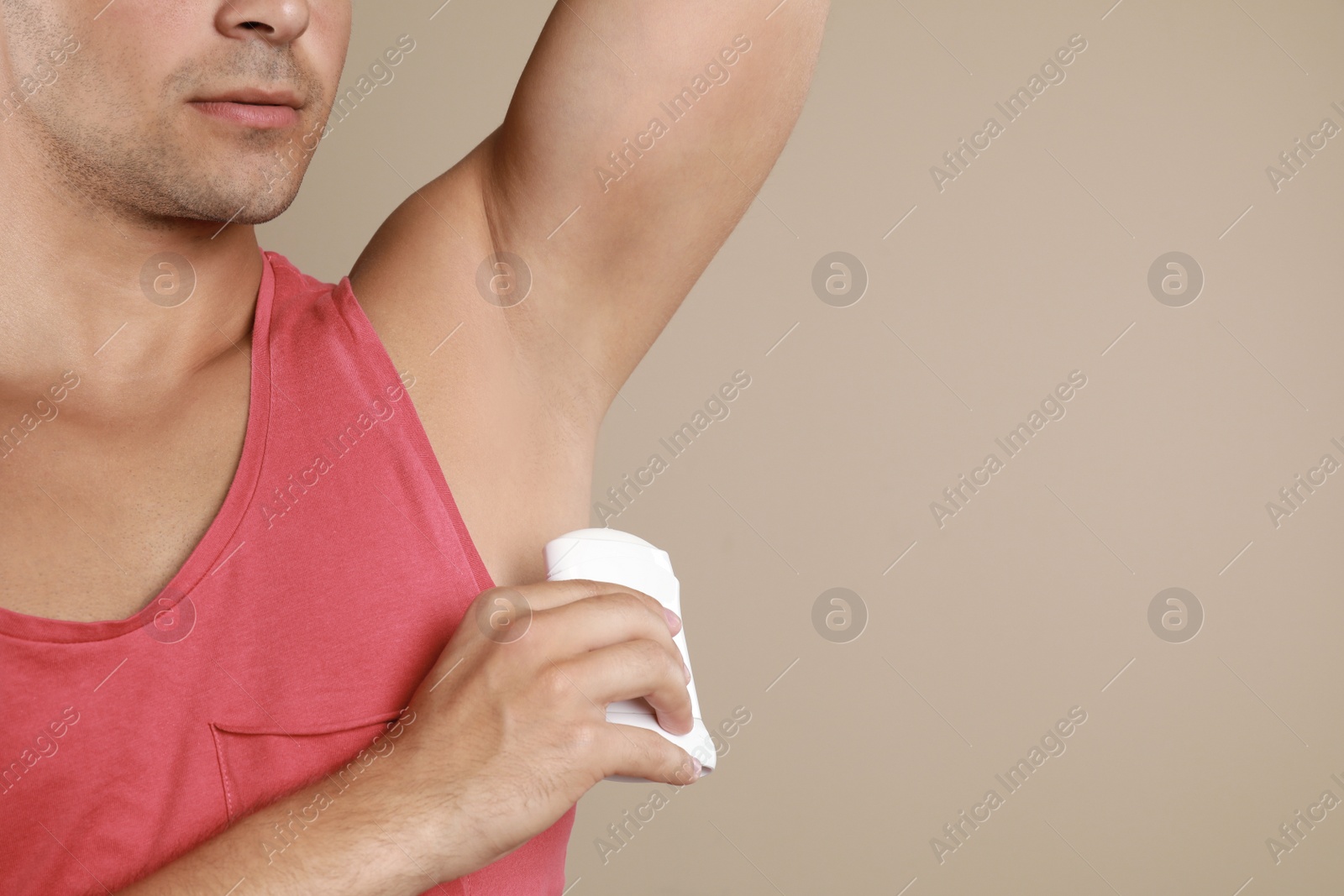 Photo of Young man applying deodorant to armpit on beige background, closeup. Space for text