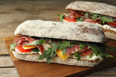 Photo of Delicious sandwich with fresh vegetables and prosciutto on wooden table, closeup