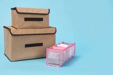 Photo of Textile storage cases and organizer with folded clothes on light blue background. Space for text