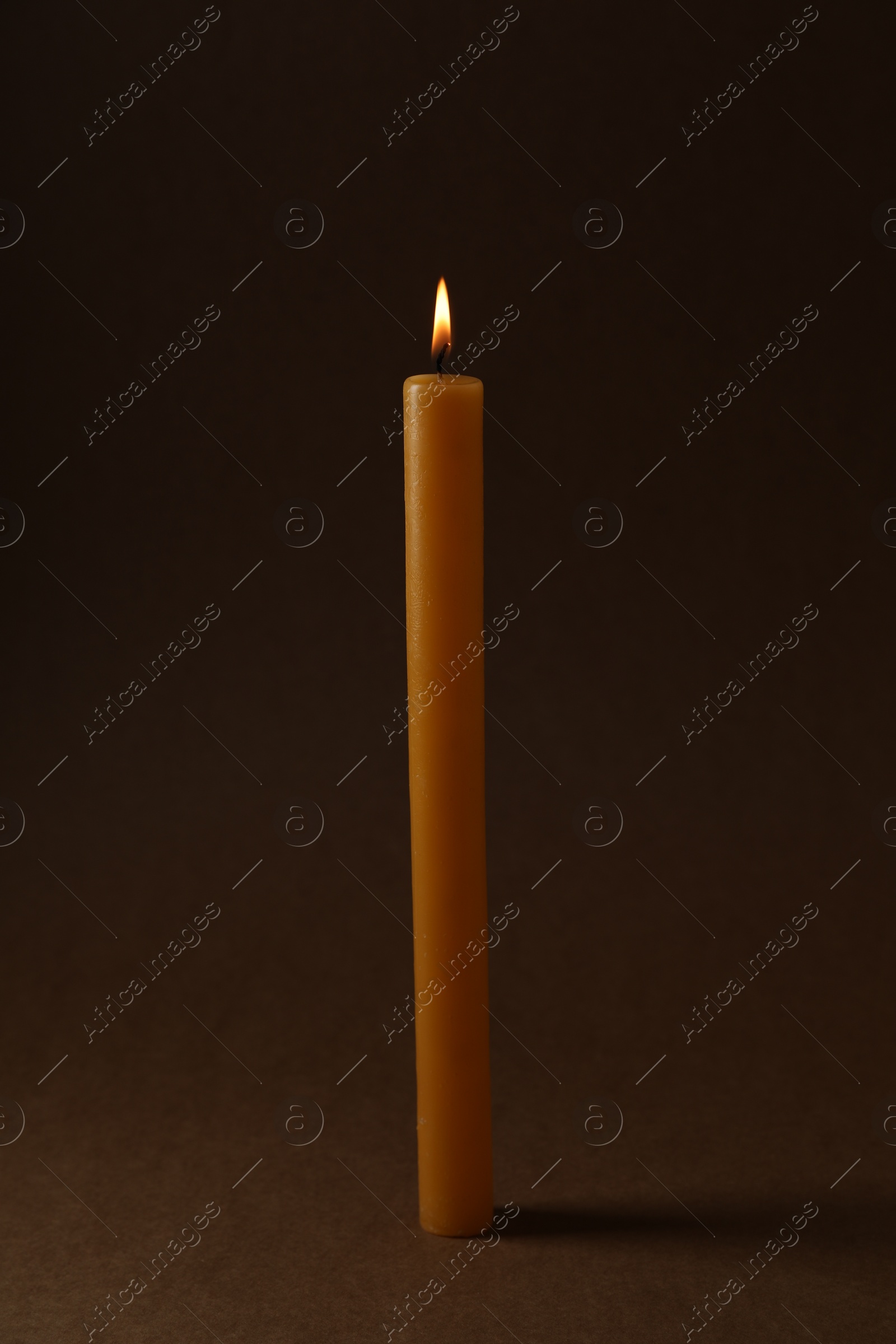 Photo of Burning church wax candle on dark background