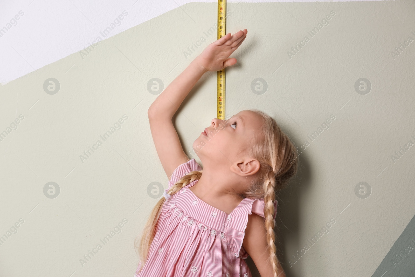 Photo of Little girl measuring her height near color wall