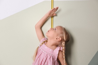 Little girl measuring her height near color wall
