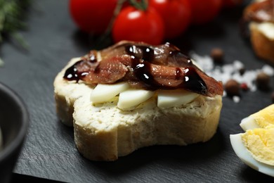 Delicious sandwich with anchovies, eggs and sauce on black table, closeup