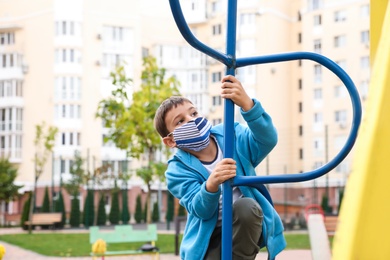 Photo of Little boy with medical face mask on playground during covid-19 quarantine