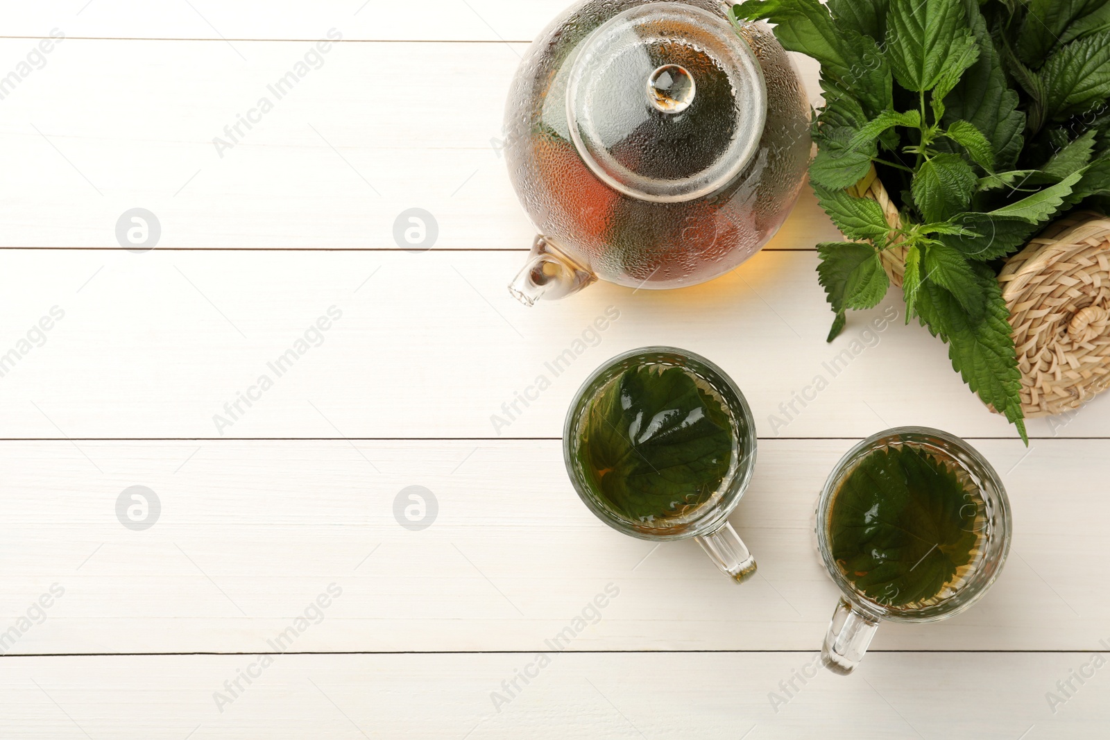 Photo of Aromatic nettle tea and green leaves on white wooden table, flat lay. Space for text