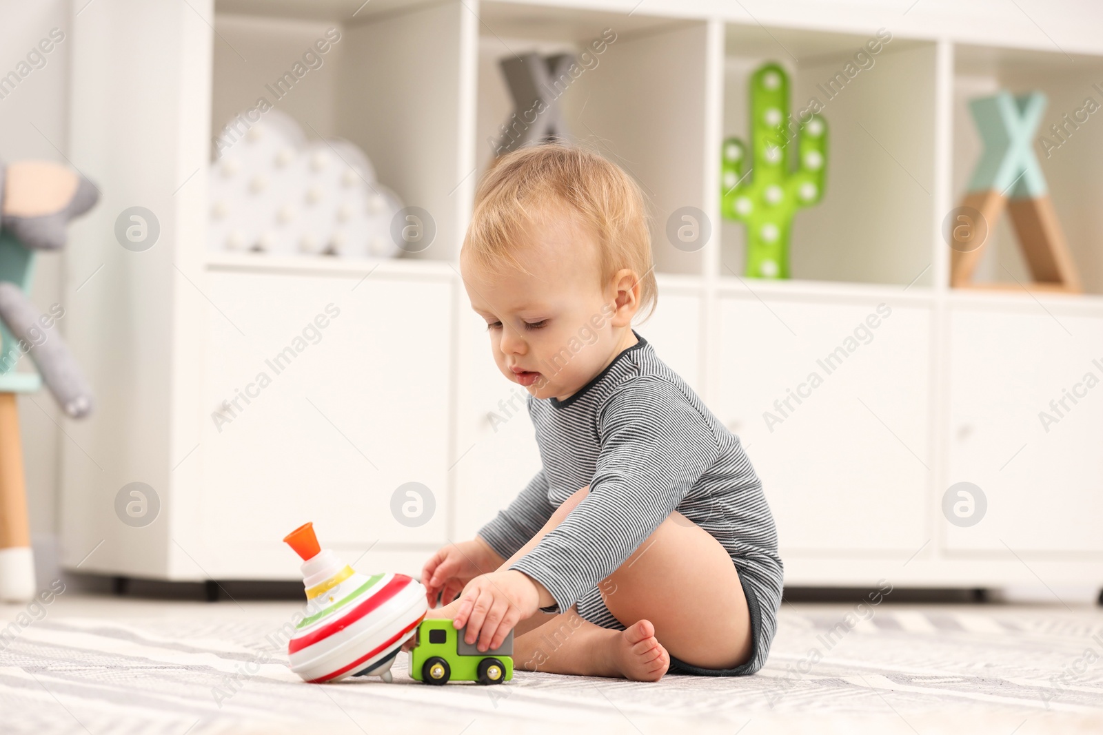 Photo of Children toys. Cute little boy playing with toy car and spinning top on rug at home