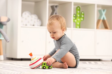 Photo of Children toys. Cute little boy playing with toy car and spinning top on rug at home