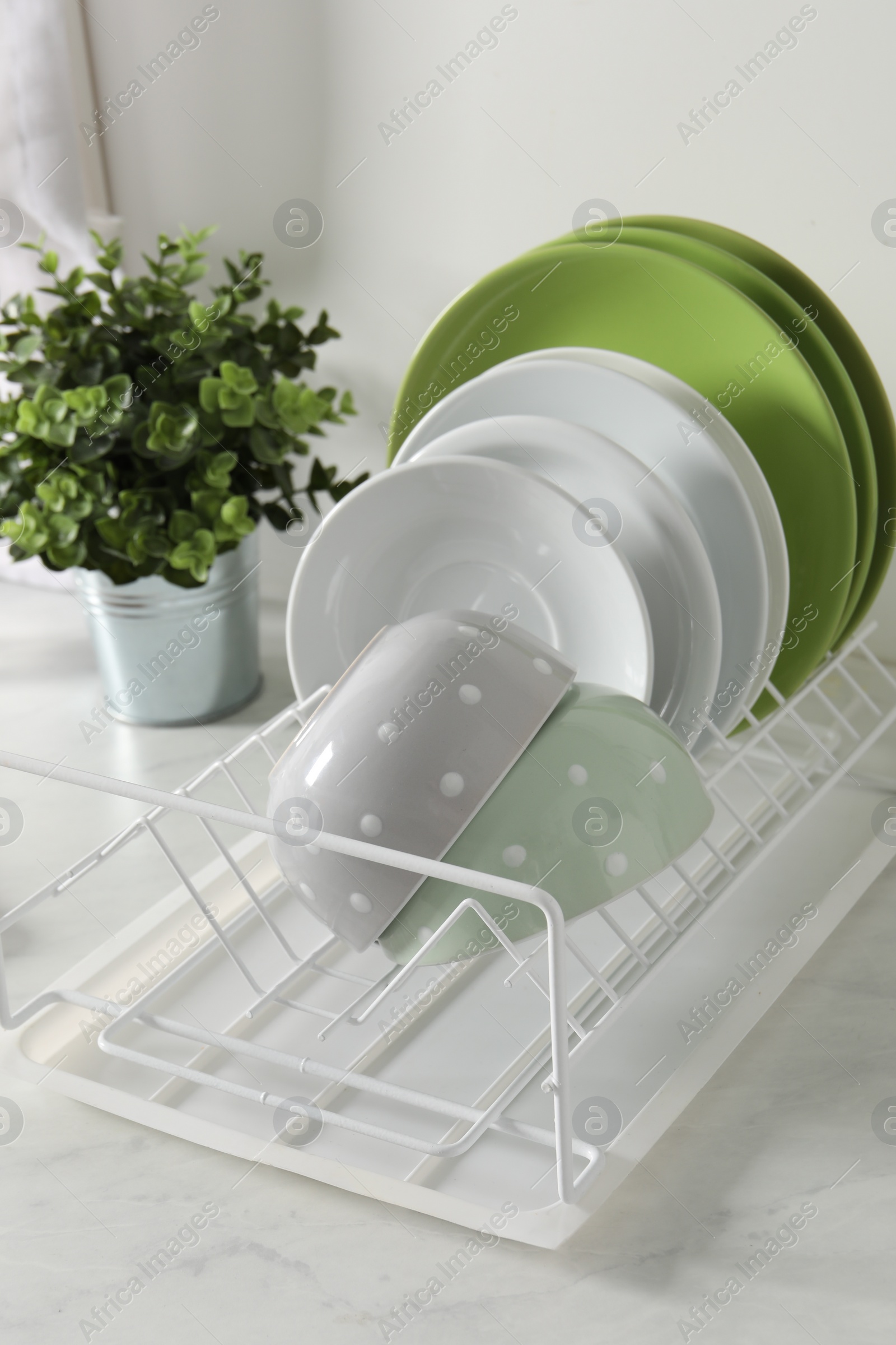 Photo of Drainer with different clean dishware and houseplant on light table in kitchen