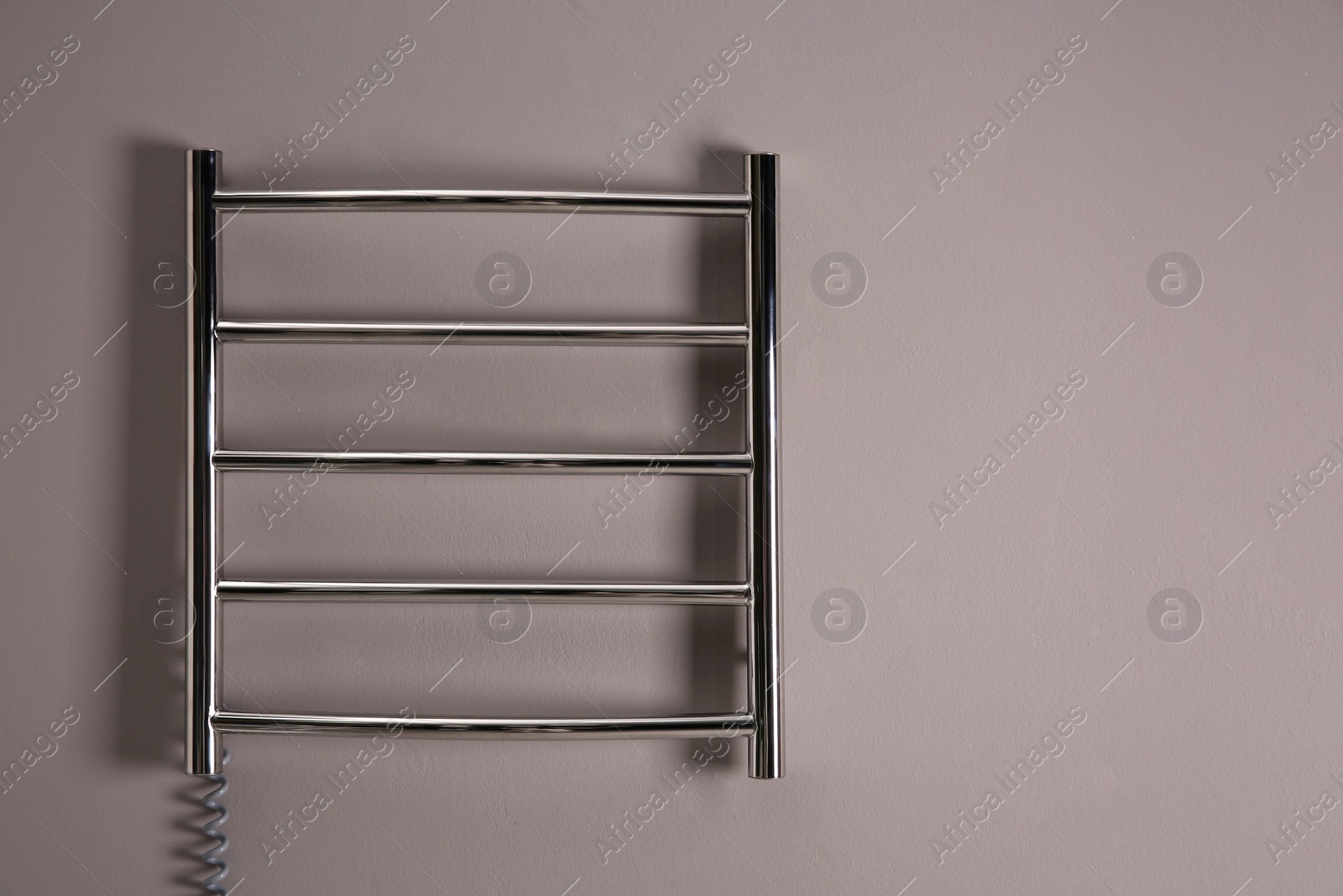 Photo of Modern heated towel rail on grey wall. Space for text