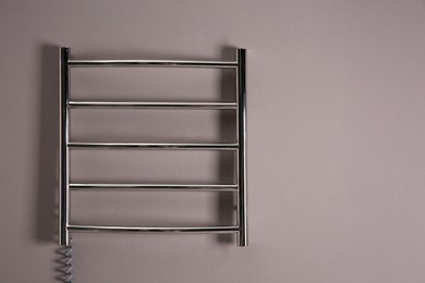 Photo of Modern heated towel rail on grey wall. Space for text