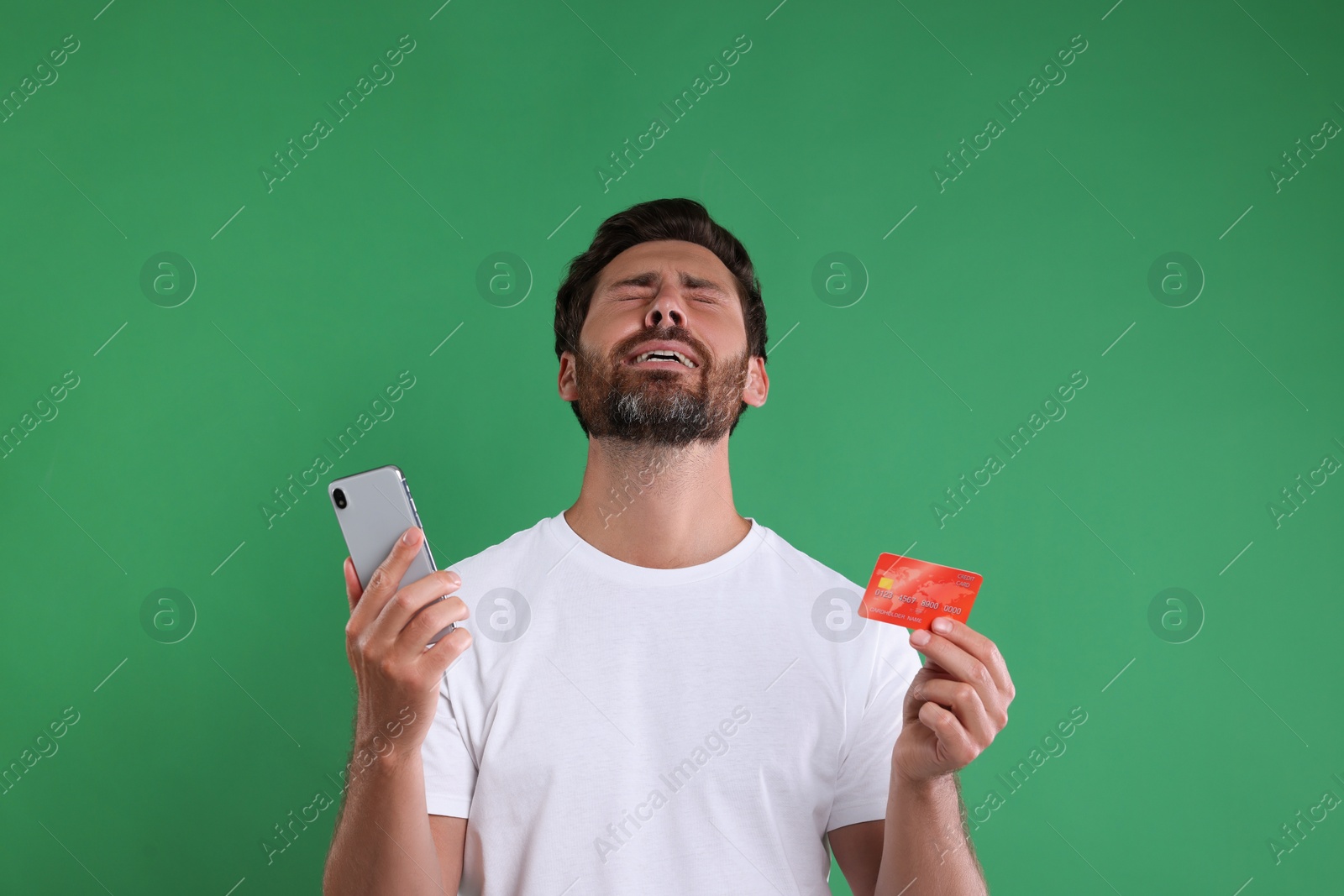 Photo of Emotional man with smartphone and credit card on green background. Be careful - fraud