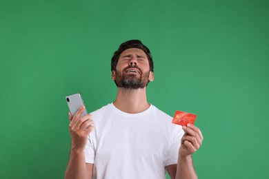Photo of Emotional man with smartphone and credit card on green background. Be careful - fraud