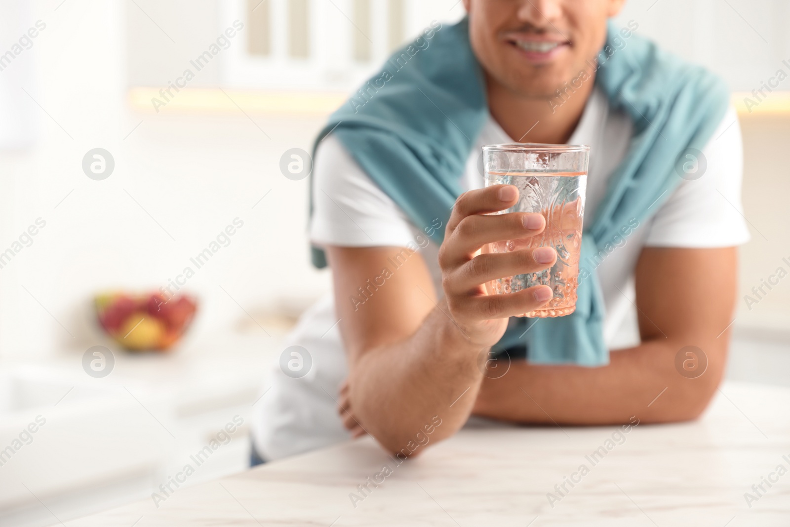 Photo of Man holding glass of pure water at table in kitchen, closeup