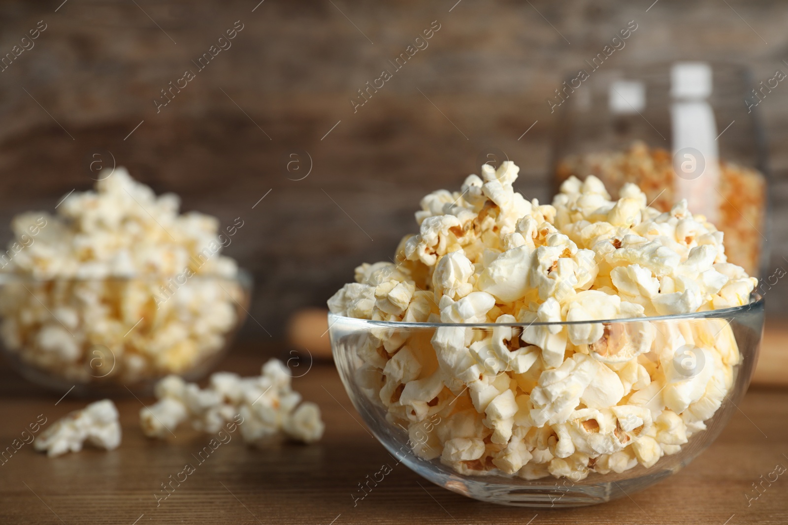 Photo of Glass bowl with tasty popcorn on table. Space for text