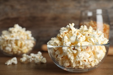 Photo of Glass bowl with tasty popcorn on table. Space for text