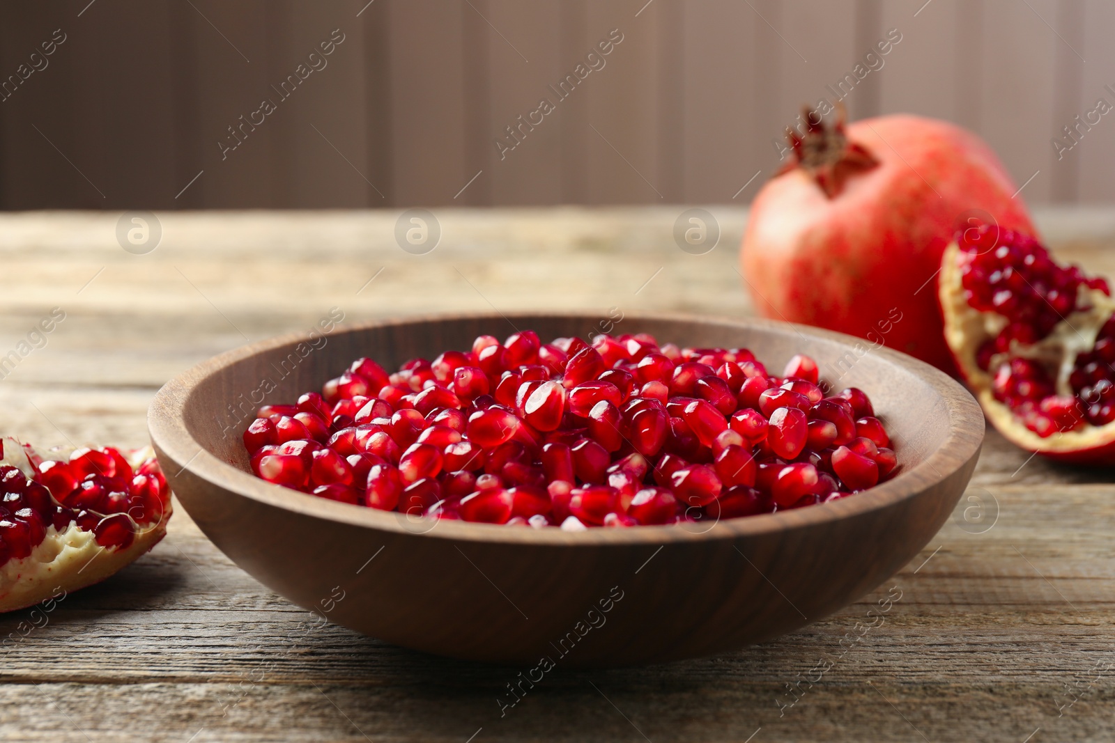 Photo of Ripe juicy pomegranate grains in bowl on wooden table, closeup