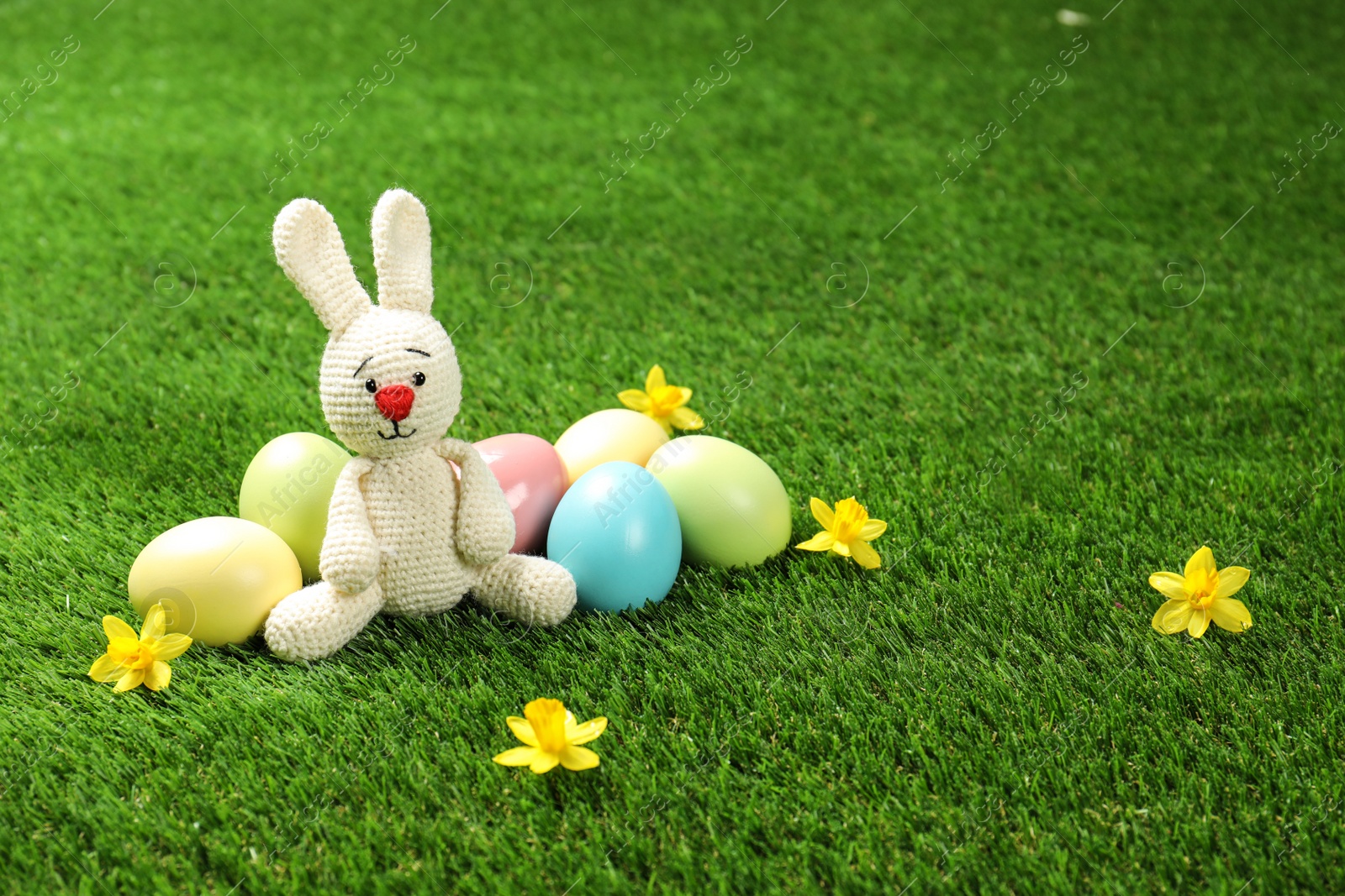 Photo of Cute Easter bunny toy and dyed eggs on green grass, space for text