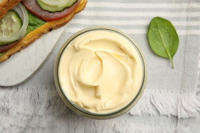 Photo of Jar of delicious mayonnaise near fresh sandwich on table, flat lay