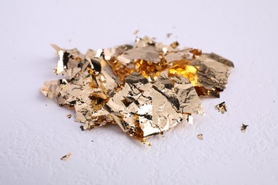 Photo of Many pieces of edible gold leaf on white textured table, closeup