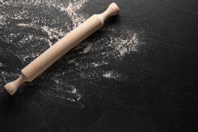 Photo of Scattered flour and rolling pin on black textured table, top view. Space for text