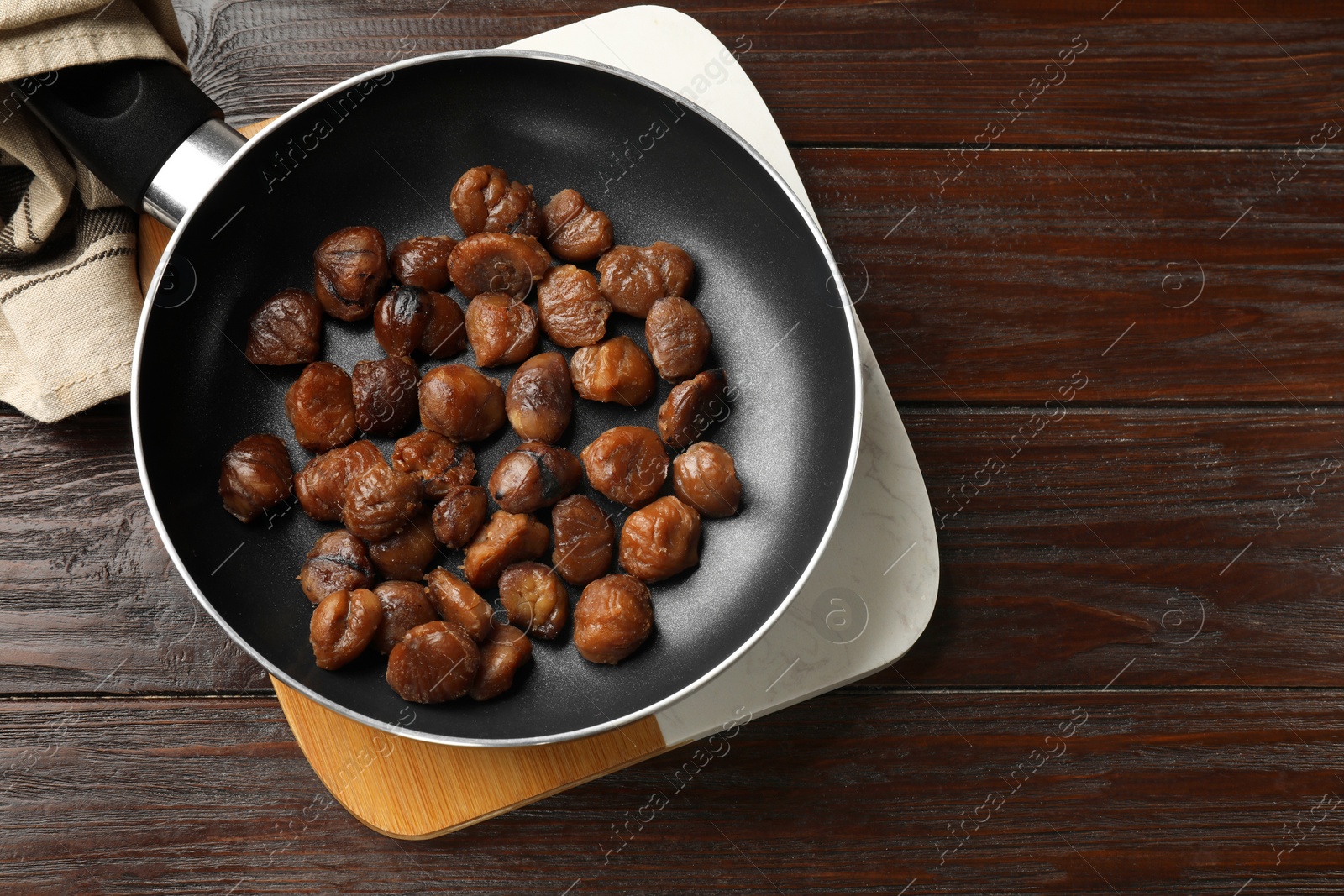 Photo of Roasted edible sweet chestnuts in frying pan on wooden table, top view. Space for text