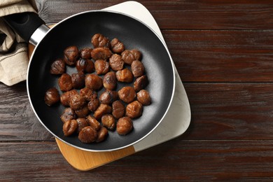 Photo of Roasted edible sweet chestnuts in frying pan on wooden table, top view. Space for text