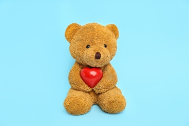 Photo of Cute teddy bear with red heart on light blue background. Valentine's day celebration
