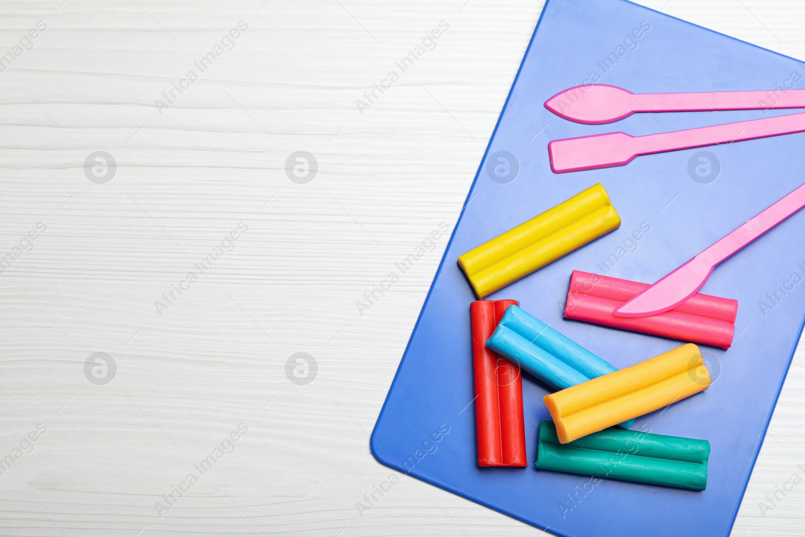 Photo of Many different colorful plasticine pieces with tools on white wooden table, top view. Space for text