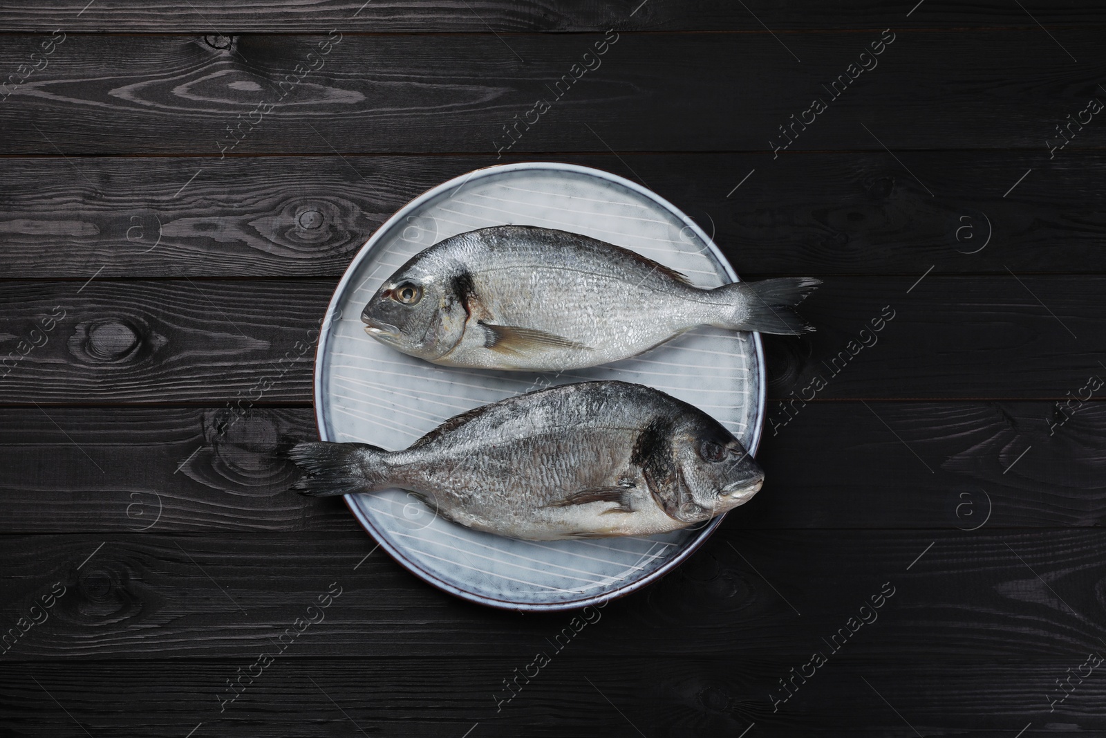 Photo of Fresh raw dorado fish on black wooden table, top view