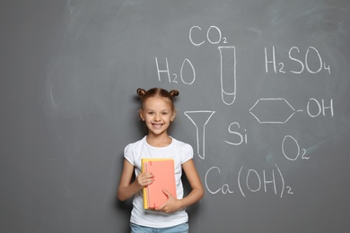 Little child with school supplies and chemical formulas on grey background