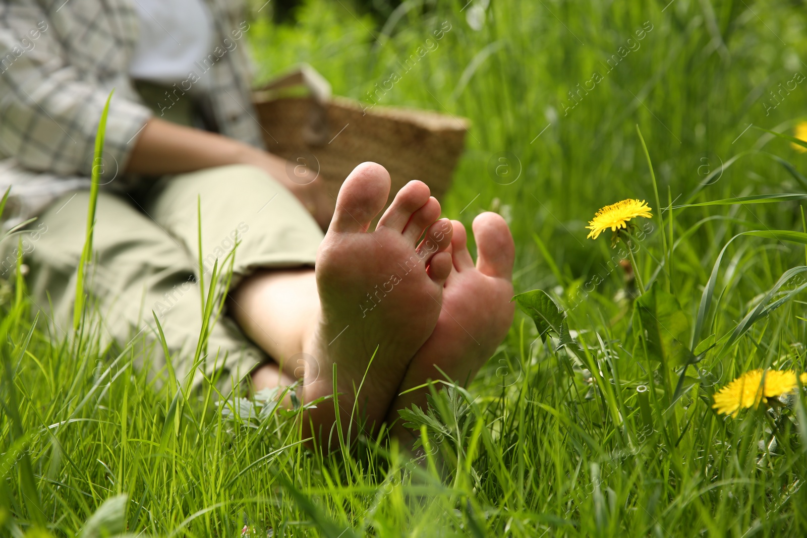 Photo of Woman sitting barefoot on green grass outdoors, closeup