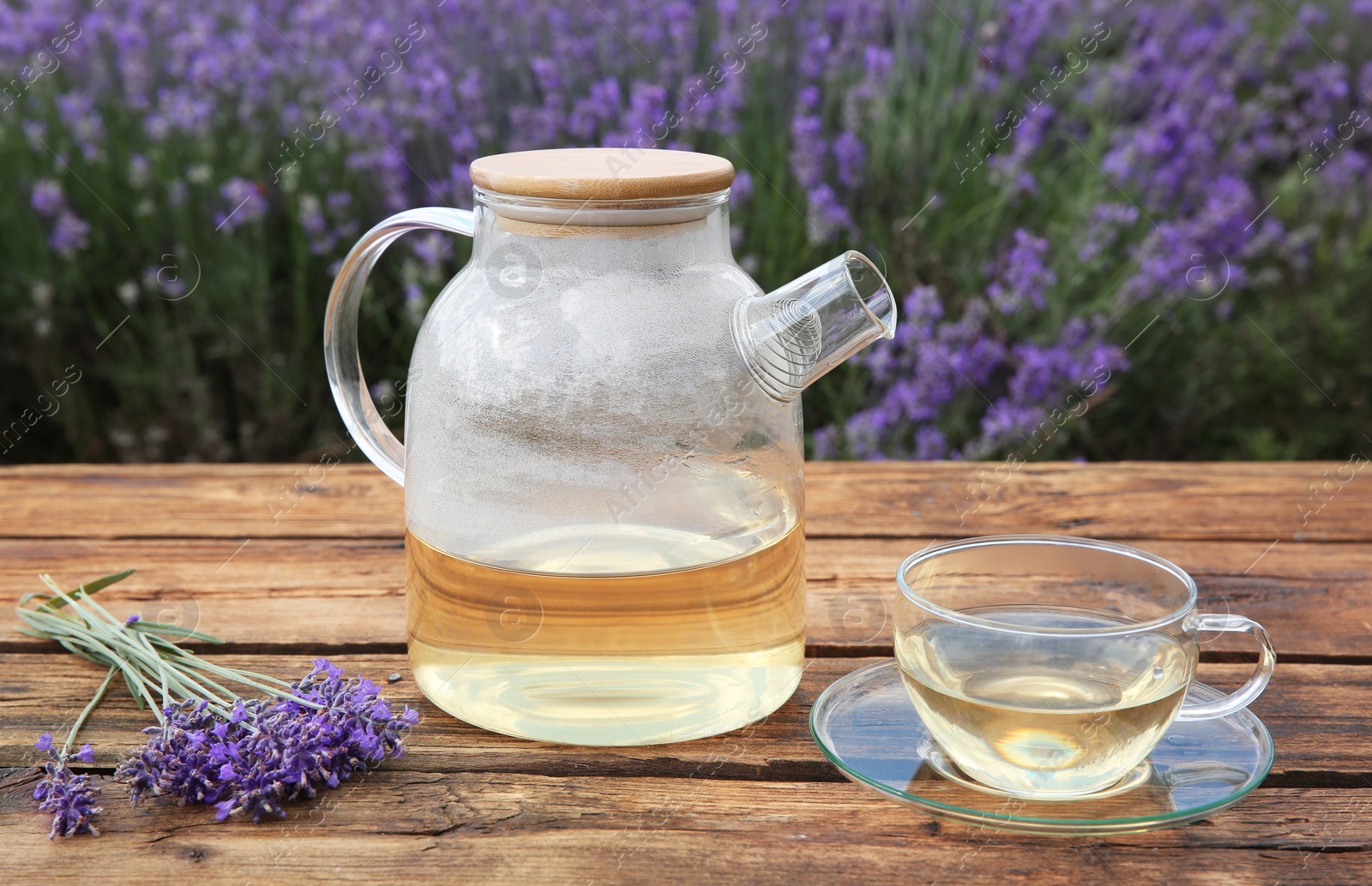 Photo of Tasty herbal tea and fresh lavender flowers on wooden table in field