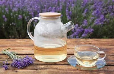 Photo of Tasty herbal tea and fresh lavender flowers on wooden table in field