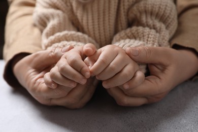 Photo of Woman holding hands with her little daughter at light grey table, closeup