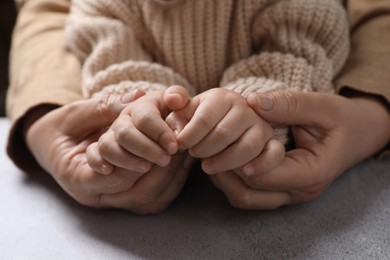 Woman holding hands with her little daughter at light grey table, closeup