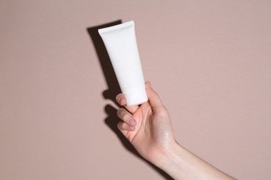 Woman with tube of cream on beige background, closeup