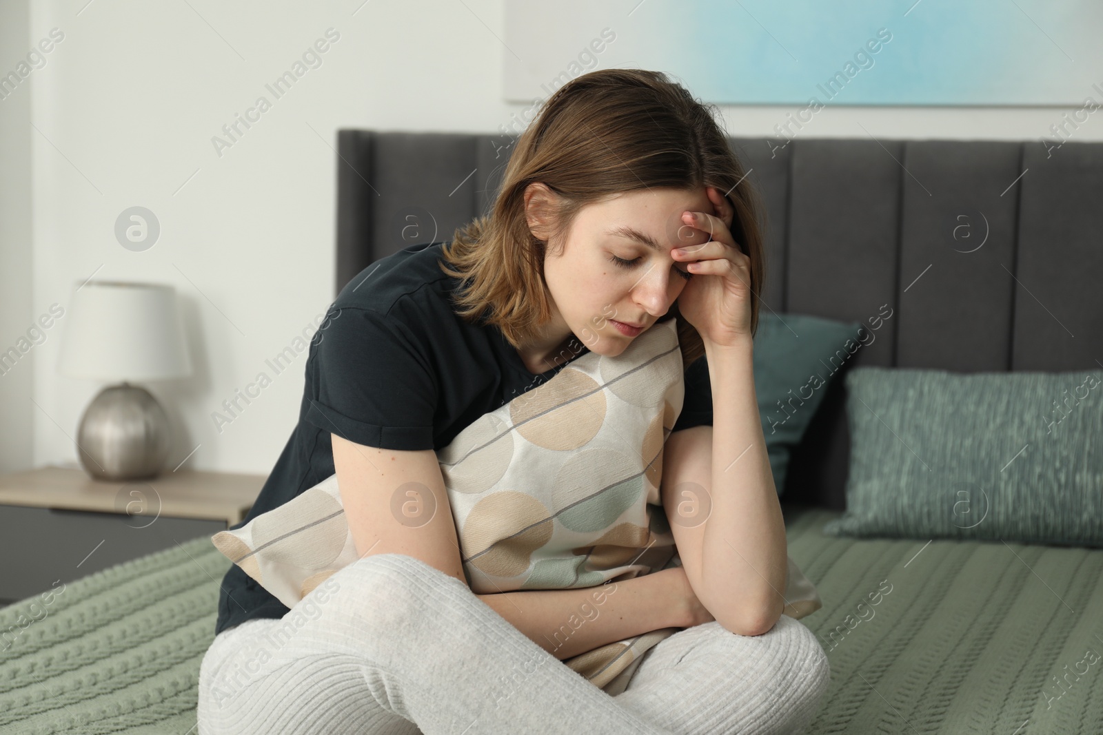 Photo of Sad young woman sitting on bed at home