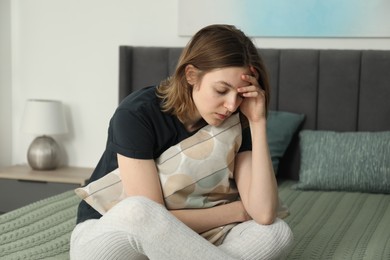 Sad young woman sitting on bed at home