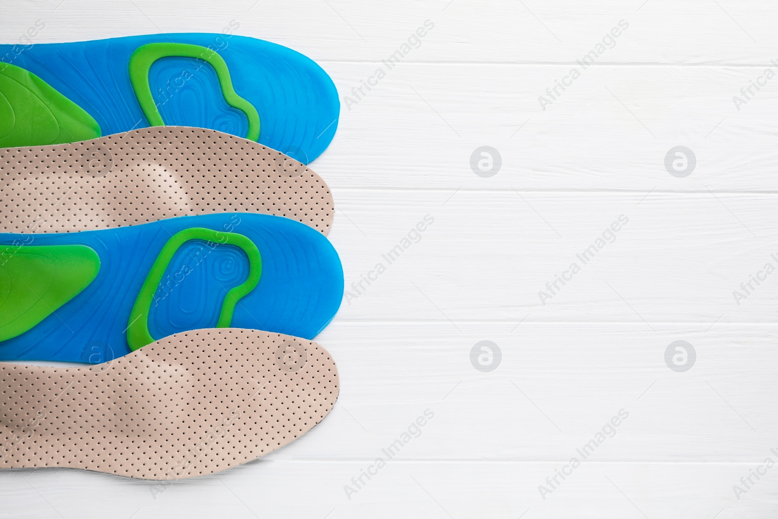 Photo of LIght blue and beige orthopedic insoles on white wooden background, flat lay. Space for text