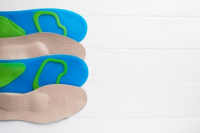 LIght blue and beige orthopedic insoles on white wooden background, flat lay. Space for text